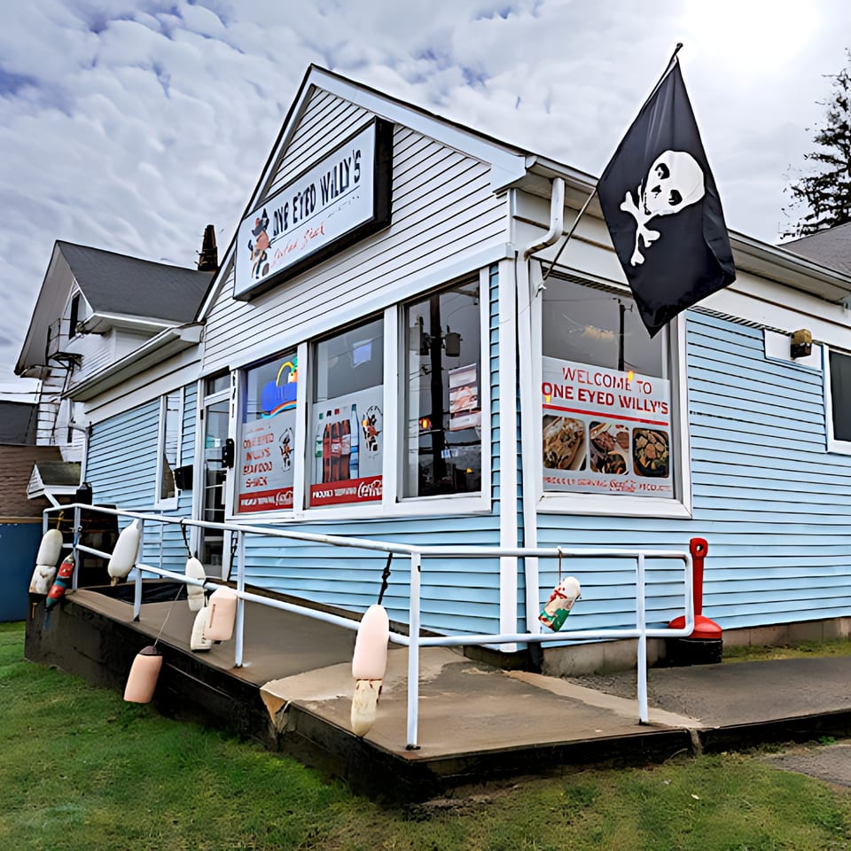 Exterior of Willy's Pub & Grub, a light blue building with a pirate flag and buoys on the railing.