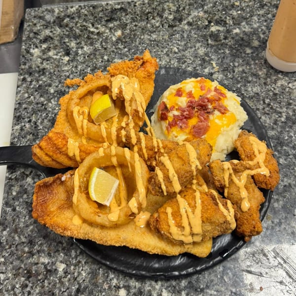 Fried fish, onion rings, and shrimp with sauce and lemon, alongside mashed potatoes with cheese and bacon.