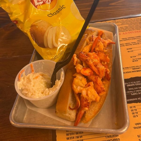A lobster roll, coleslaw, and a bag of Lay's potato chips on a metal tray.