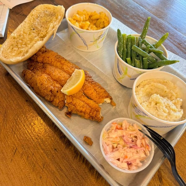 Fried fish fillets with a lemon wedge, green beans, mac and cheese, coleslaw, and a bun.