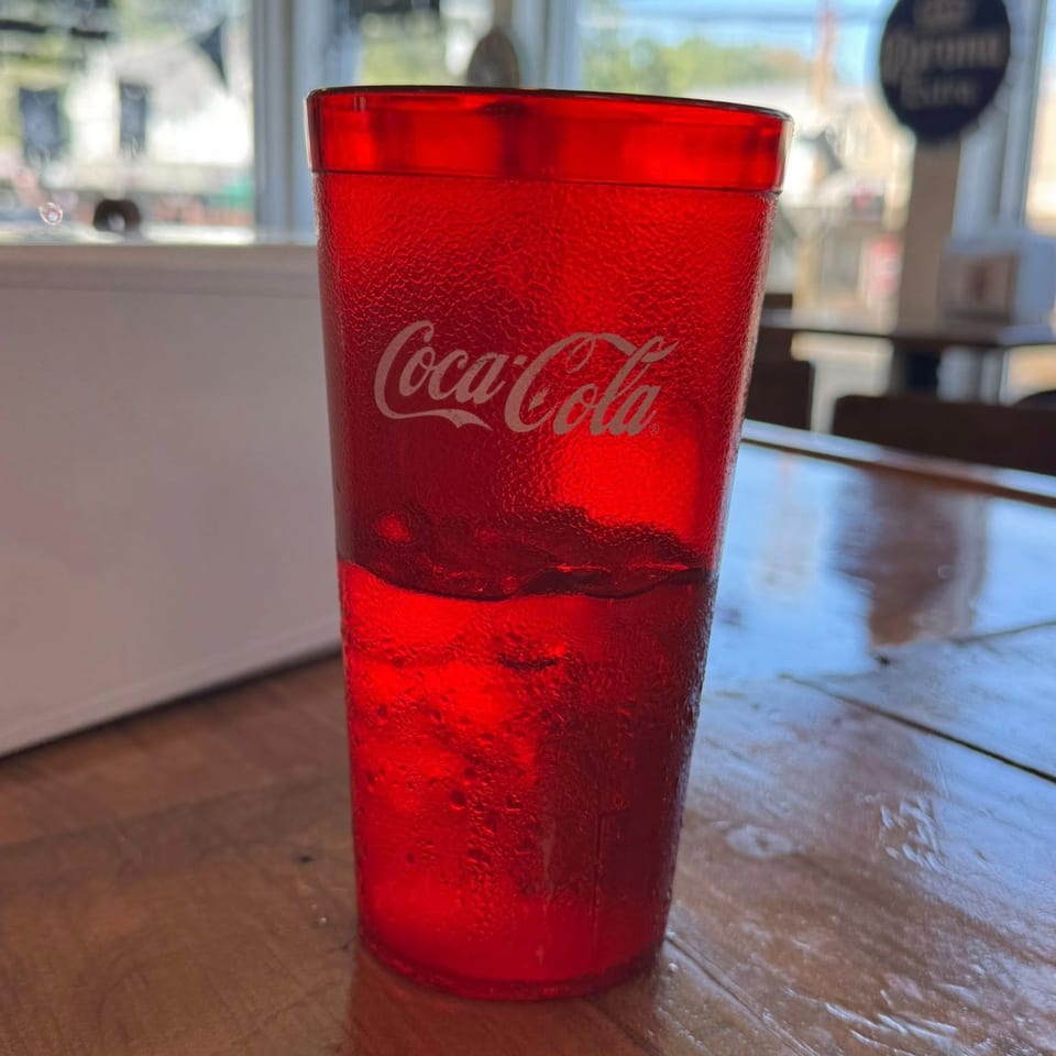 A red Coca-Cola cup filled with ice and a drink, sitting on a wooden table.